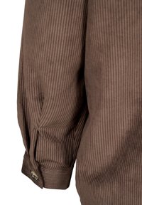 Manche de chemise en velours marron avec poignet boutonné visible et texture côtelée verticale.