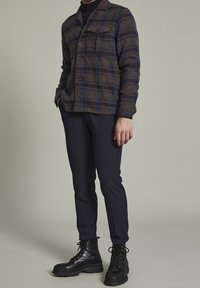 Brun och blå rutigt ullskjortjacka med krage, framfickor och tre knappar, kombinerad med marinblå slim-fit byxor och svarta snörskor.