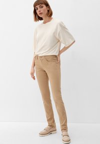 Beżowe bawełniane spodnie o dopasowanym kroju z przednimi kieszeniami, zestawione z luźną, kremową koszulą z krótkim rękawem i beżowymi butami wsuwanymi.