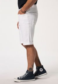 Pantalones cortos de mezclilla blanca con dobladillos enrollados, que cuentan con bolsillos frontales y un ajuste slim. Llevados con zapatillas altas en color navy y tatuajes visibles en las piernas.