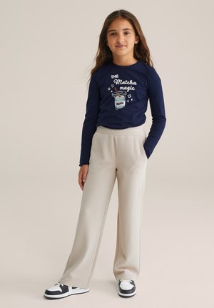 Marineblaue Langarm-T-Shirt mit "Matcha Magic" Grafik, kombiniert mit hellbeigen strukturierten weit geschnittenen Hosen und schwarz-weißen Turnschuhen.