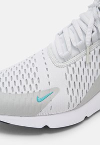 Vit träningsskor med ett andningsbart mesh-övre som har grå accenter, en ljusblå logotyp och en flexibel vit sula.