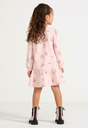 Vestito rosa con motivo di torte e dolci, orlo arricciato e maniche lunghe, abbinato a stivaletti neri e rosa alla caviglia.