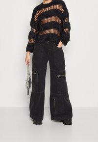 Black, oversized knitted sweater with sheer stripes and fuzzy texture. Black wide-leg cargo pants with pockets and zippers. Silver chain accessory.