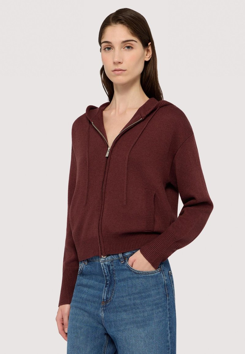 Mörkröd zip-up hoodie i texturerad stickad tyg, med en huva, framfickor och ribbade ärmslut, kombinerad med blå jeans.