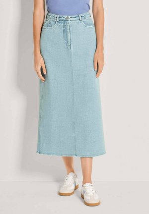 Frau trägt einen hellblauen Denim-Midirock mit Fronttaschen, kombiniert mit weißen Sneakern und einem in den Rock gesteckten blauen Oberteil.