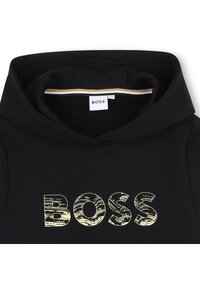 Črna kapuca z zaznanim teksturiranim rumenim logotipom "BOSS" na sprednji strani, s podloženim kapuco, ki prikazuje kontrastno zlato in črno črto.