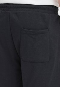 Mustad puuvillased dressipüksid elastse vöökohaga, millel on ainult üks tagatasku paremal küljel ning sile ja pehme tekstuur.