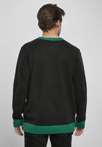 Pulover tricotat negru cu guler și tiv verde. Prezintă o croială lejeră și un material texturat. Vedere din spate.