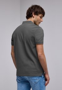 Polo shirt gris foncé à manches courtes, en coton, avec un col classique et des fentes sur l'ourlet. Porté avec un jean bleu clair.