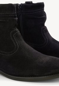 Bottines en daim noir avec fermeture à glissière latérale, coutures décoratives et languette boucle sur le dessus de la tige.