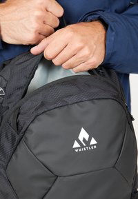 Svart ryggsäck med en geometrisk design, utrustad med ett dragkedjeöppning, logotyp och texturerad yta. Materialet verkar vara hållbart och väderbeständigt.