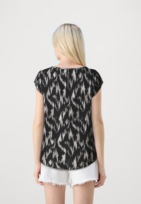 Zwarte en beige geblokte top met korte mouwen, ronde zoom en ritsdetail op de rug, in combinatie met witte gescheurde shorts.