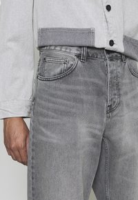 Jasnoszare jeansy z denimu o klasycznym kroju, z pięcioma kieszeniami, delikatnym przetarciem i tonowaną nicią, zestawione z jasnoszarą koszulą zapinaną na guziki.