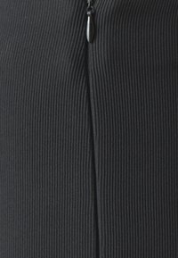 Tissu noir à côtes avec un détail de fermeture éclair discret. La texture est lisse avec des lignes verticales, créant une apparence structurée.