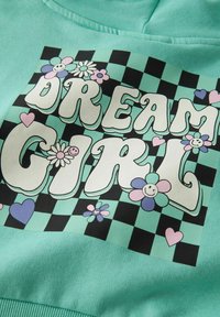 Mintroheline dressipluus suures graafikas, kus valge tekst "DREAM GIRL" on ümbritsetud värviliste lillede ja südametega ruudulises taustas.