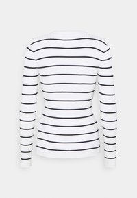 Top a maniche lunghe a costine bianco con righe orizzontali blu navy. Presenta una silhouette aderente e un collo rotondo.