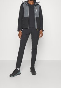 Veste noire avec accents gris, fermeture éclair et capuche ; associée à un pantalon noir et des chaussures noires avec des détails turquoise, adaptée aux activités en plein air.