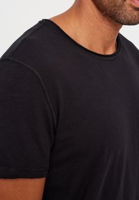 Svart T-shirt med rund halsringning, korta ärmar och synlig sömnad. Tyget verkar mjukt med en slät yta.