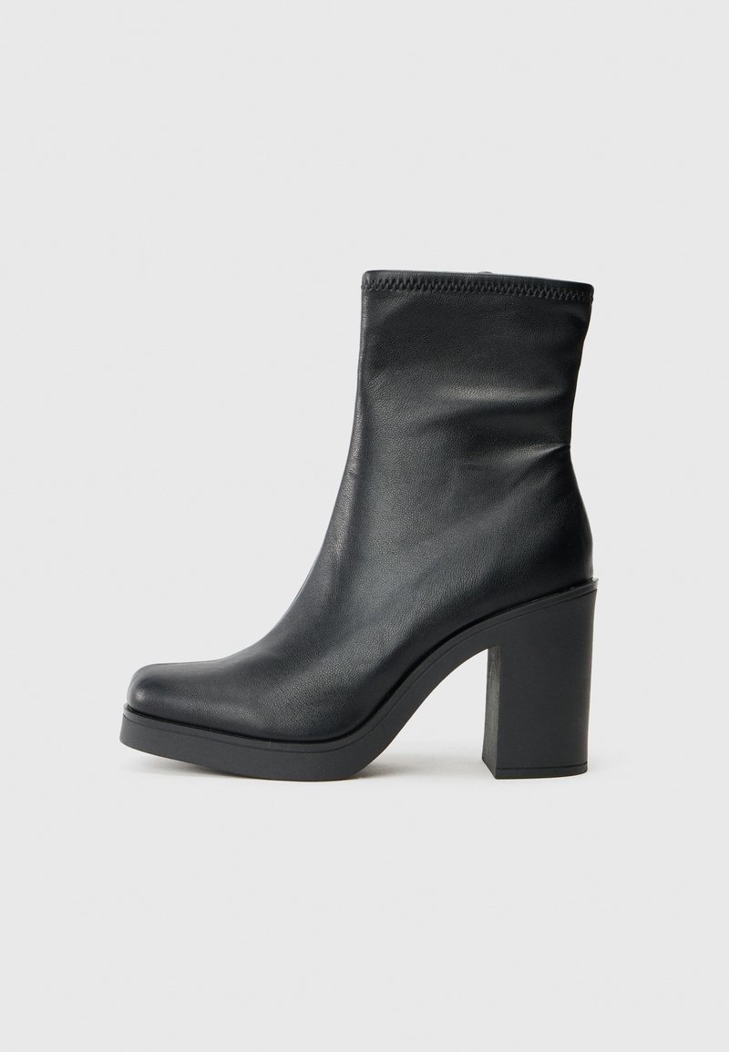 Schwarze Lederknöchelstiefel mit hohem Blockabsatz, glatter Textur, enganliegendem Design und genähten Details am oberen Rand.