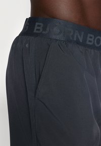 Tamno sive sportske kratke hlače s širokim pojasom na kojem je natpis "BJØRN BORG", teksturirana tkanina i bočne džepove.