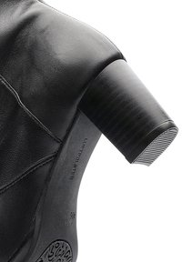 Gros plan sur une chaussure à talon bloc en cuir noir montrant une semelle texturée et des coutures sur le dessus du matériau.