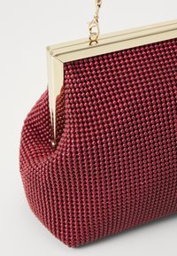 Clutch rossa con perline, dotata di una struttura in metallo e di una catena removibile. La forma arrotondata, la superficie texturizzata e la finitura lucida ne esaltano l'appeal visivo.