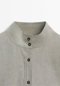 Col de chemise gris clair avec un col en bande et cinq boutons foncés au centre devant sur un fond blanc uni.