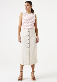 Top sans manches blanc avec des rayures ondulées roses, associé à une jupe midi beige avec des boutons à l'avant et un ourlet effiloché. Sandales à talons compensés marron.