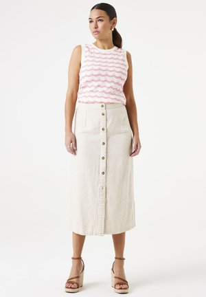 Witte mouwloze top met roze golvende strepen, gecombineerd met een beige midi-rok met knopen aan de voorkant en een franjezoom. Bruine plateau-sandaaltjes.