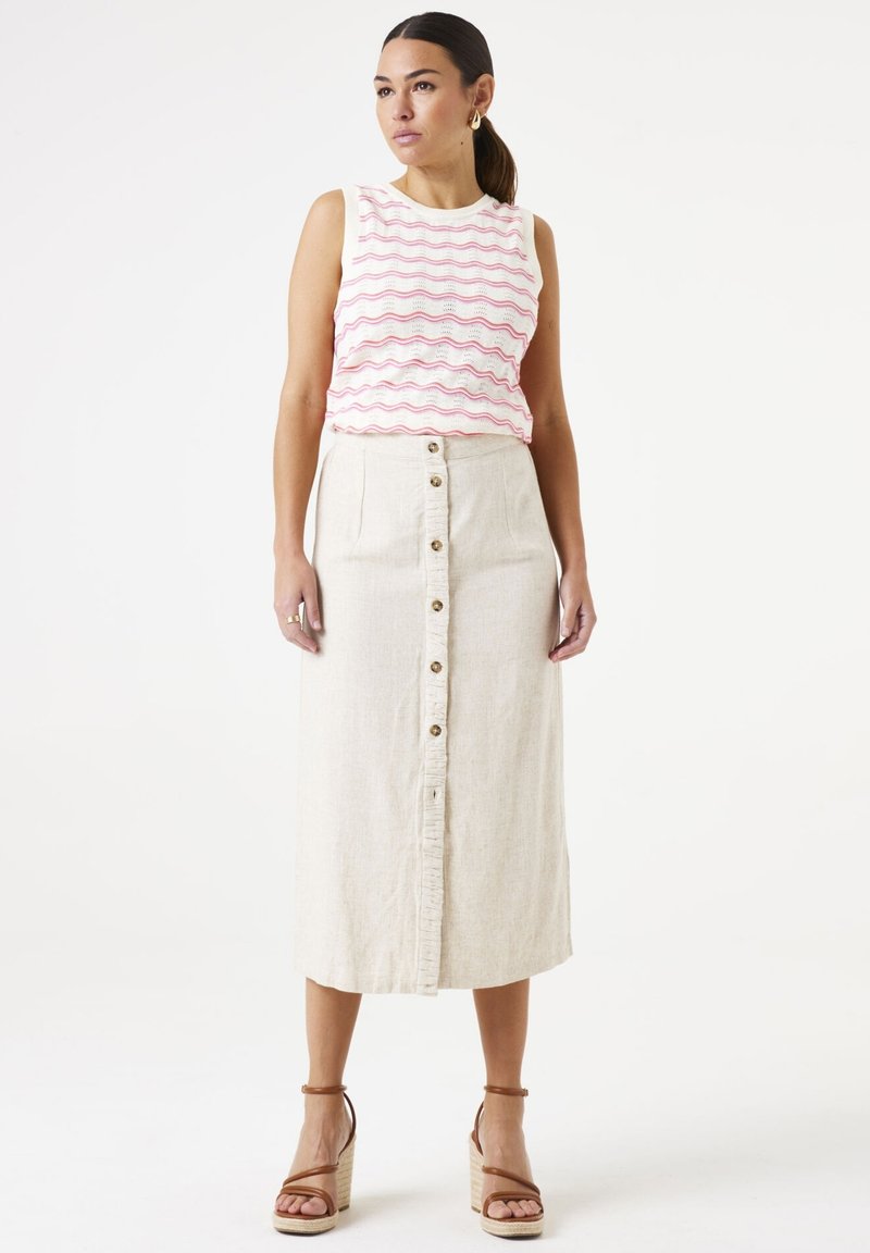 Top sans manches blanc avec des rayures ondulées roses, associé à une jupe midi beige avec des boutons à l'avant et un ourlet effiloché. Sandales à talons compensés marron.