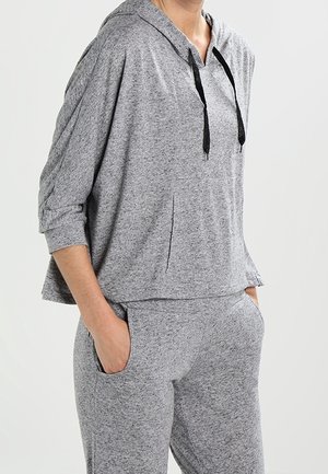 Grijze sweat met capuchon, losse pasvorm, verlaagde schouders en een zak aan de voorkant. Gecombineerd met bijpassende grijze joggers met zijzakken.