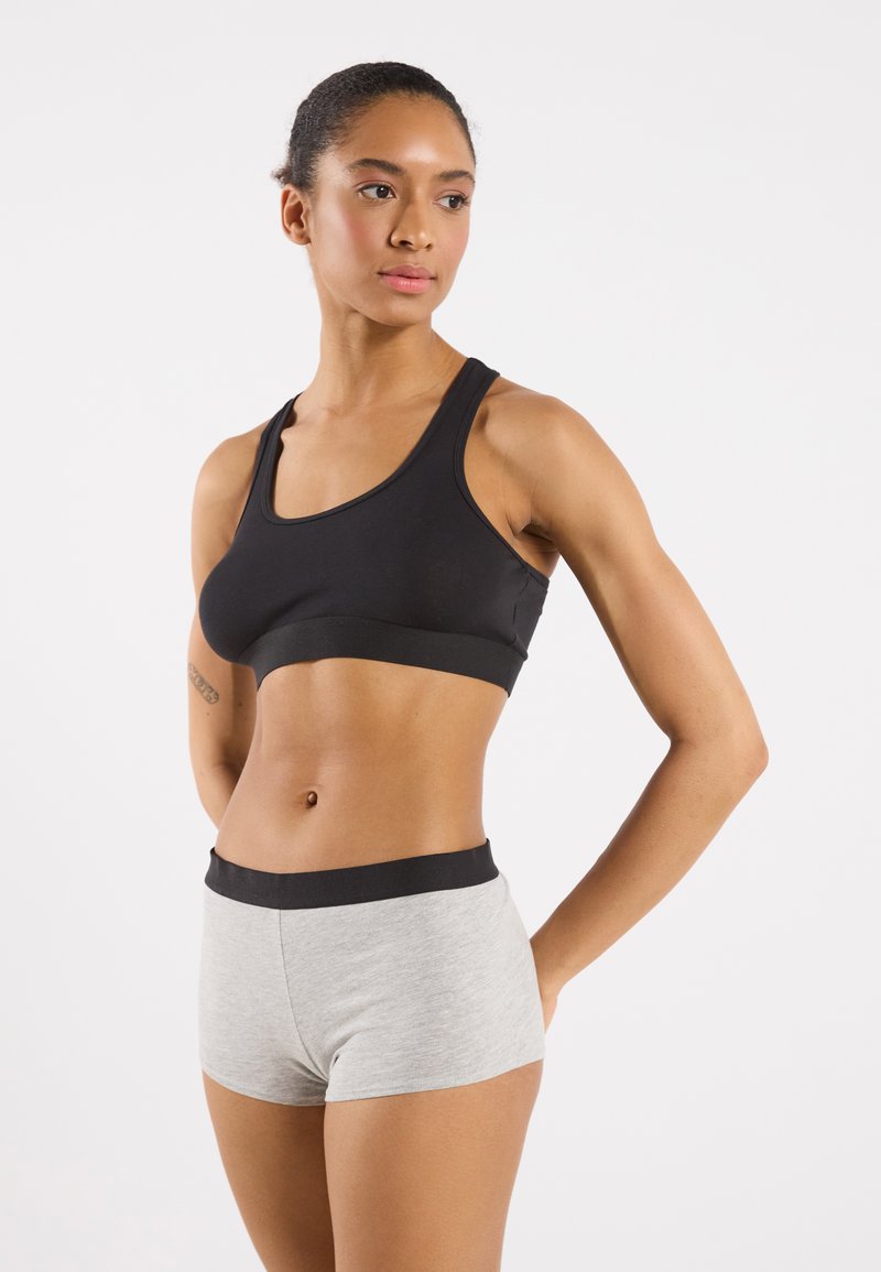 Soutien-gorge de sport noir avec de larges bretelles et une finition lisse, associé à un short en legging gris avec une taille élastique noire.
