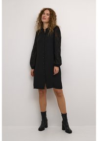 Black button-up dress with long sheer lace sleeves, a relaxed fit, and a straight silhouette, paired with knee-high black heeled boots.