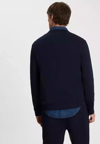 Granatowy sweter z ribbowym wykończeniem na dole i przy mankietach, z okrągłym dekoltem i dopasowanym krojem. Na plecach noszony na niebieskiej koszuli dżinsowej.