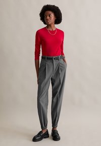 Czerwona bluzka z długim rękawem połączona z szarymi spodniami w prążki o zwężanym kroju; czarne skórzane mokasyny z grubą podeszwą oraz regulowany pas z klamrą.