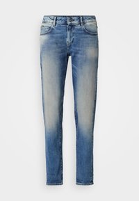 Jean slim bleu délavé avec poches avant, fermeture à boutons et détails subtils d'usure sur la partie supérieure de la cuisse.