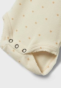 Krämfärgad baby bodysuit med ribbat mönster som har små bruna hjärtan, tryckknappar i botten och texturerad kant runt kanterna.
