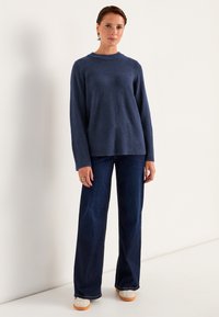 Marineblauer Strickpullover mit Rundhalsausschnitt und geripptem Saum, kombiniert mit weit geschnittenen dunkelblauen Jeans und weißen Sneakers mit sandfarbenen Sohlen.