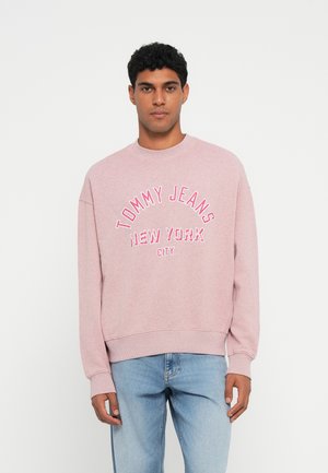 Svetlo ružová mikina s okrúhlym výstrihom, ozdobená bielym a ružovým vyšitým nápisom "TOMMY JEANS NEW YORK CITY." Voľný strih s rebrovanými manžetami.