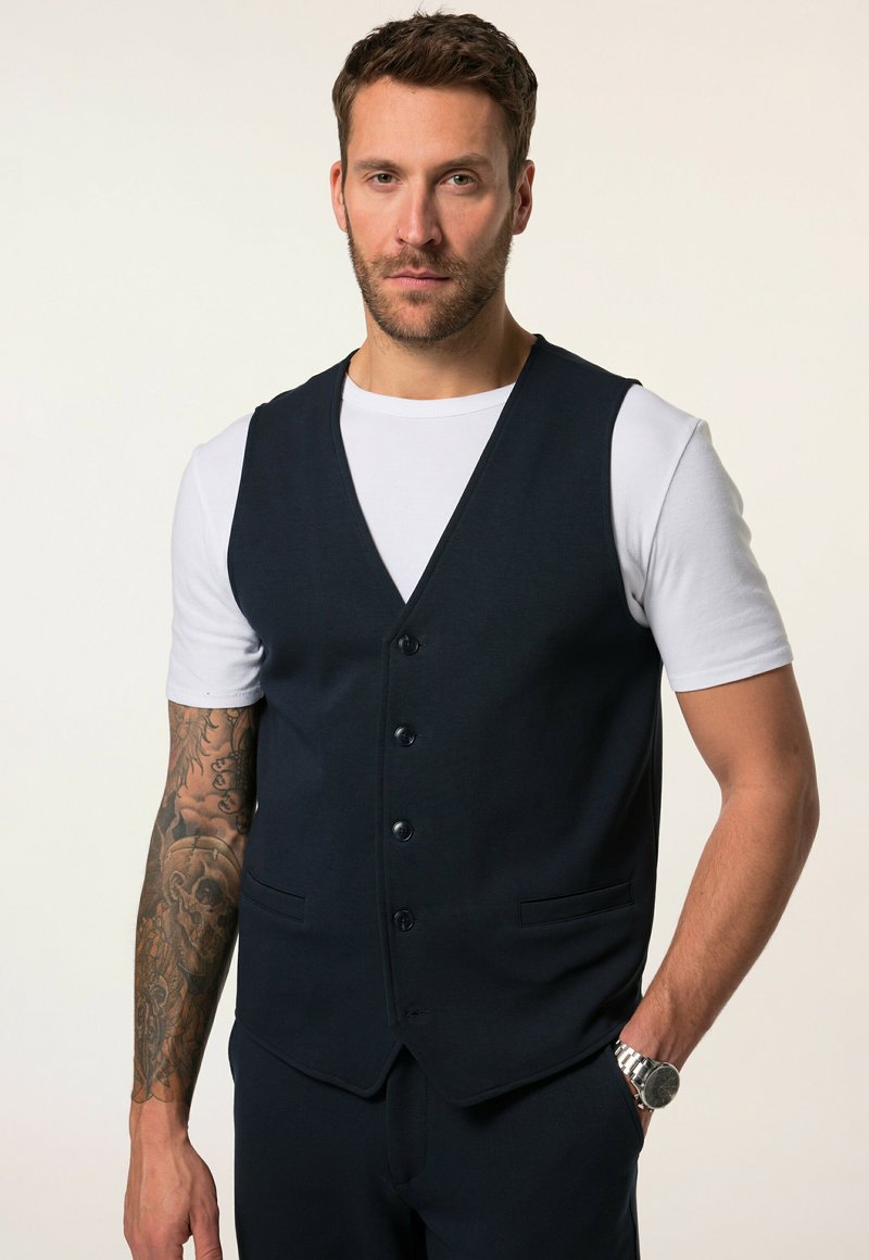 Gilet blu navy con una vestibilità aderente, design monopetto, cinque bottoni e due tasche laterali, indossato sopra una maglietta bianca.