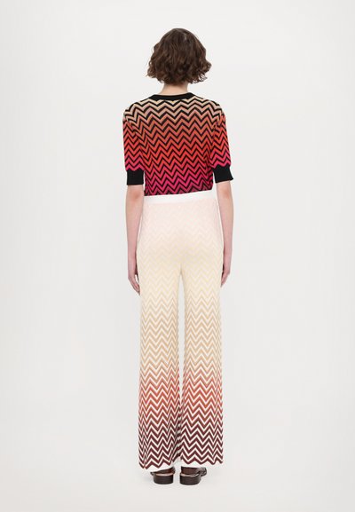Débardeur court en tricot multicolore avec un motif en chevrons rouge et noir, associé à un pantalon large avec un design en dégradé de chevrons allant de crème à bordeaux.