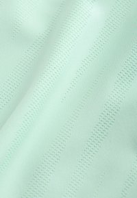 Svetlozelená látka s textúrovanými diagonálnymi pruhmi vytvorenými z malých perforácií a vystúpených pletených vzorov.