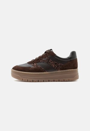 Χαμηλό sneaker με καφέ σουέντ, μαύρο δέρμα, λαμπερές λεπτομέρειες και παχύ, ανοιχτό καφέ ελαστικό πάτο σε λευκό φόντο.