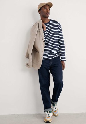 Conjunto informal que incluye una camisa de rayas azul marino y blanca de manga larga, un blazer beige, jeans oscuros y zapatillas multicolor.