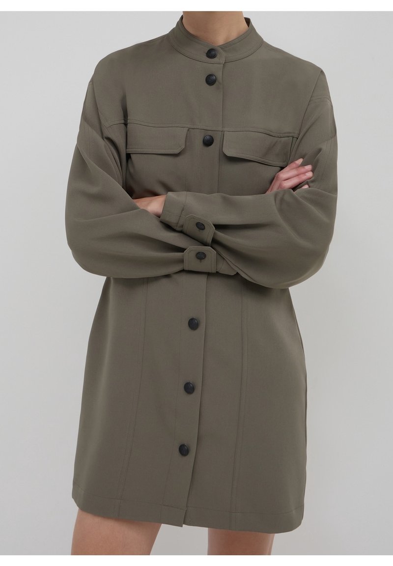 Robe olive verte à col mandarin, avec deux poches avant, manches longues et boutons noirs. Tissu lisse et coupe décontractée.