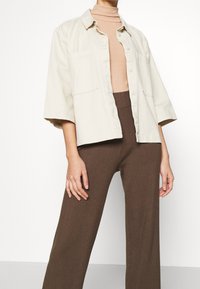 Ljusbeige knapp-up skjorta med korta ärmar, två bröstfickor, i kombination med ribbade bruna byxor. Slät textur, avslappnad design.