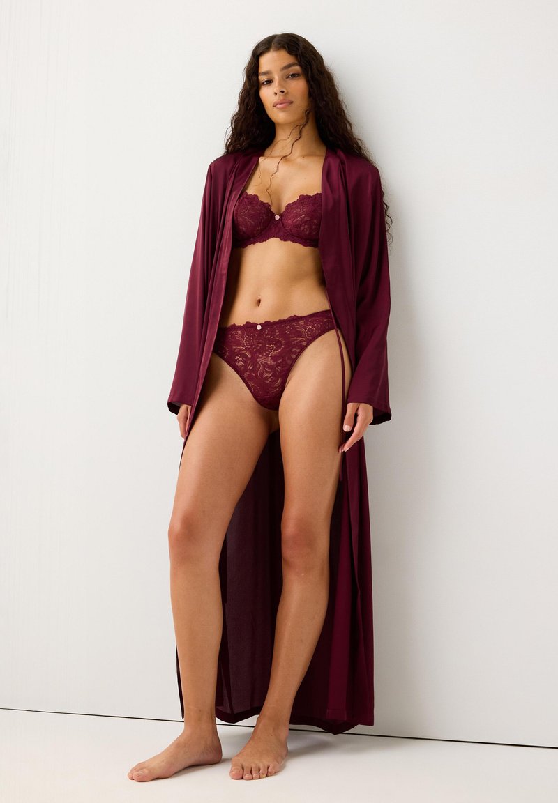 Conjunto de sujetador y bragas de encaje burdeos combinado con una bata larga y elegante de color burdeos. La bata es suave, tiene un diseño fluido y un frente abierto.