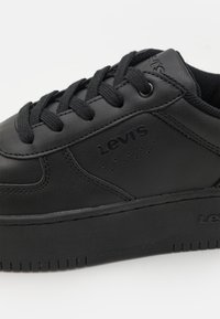 Baskets en cuir noir avec surface texturée, bout rond et semelle en caoutchouc crantée. Dotées de lacets noirs et d'un logo embossé sur le côté.