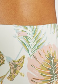 Roupa de banho em tecido leve com uma base branca e padrão colorido de folhas tropicais em verde, rosa e dourado. Inclui uma pequena etiqueta de logótipo rosa.
